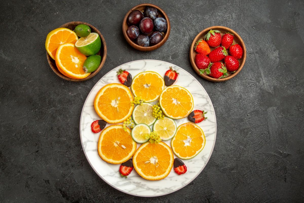 top-close-up-view-fruits-on-table-chocolate-covered-strawberries-lemon-and-orange-in-white-plate-next-to-citrus-fruits-and-berries-in-bowls-in-the-center-of-the-dark-table.jpg