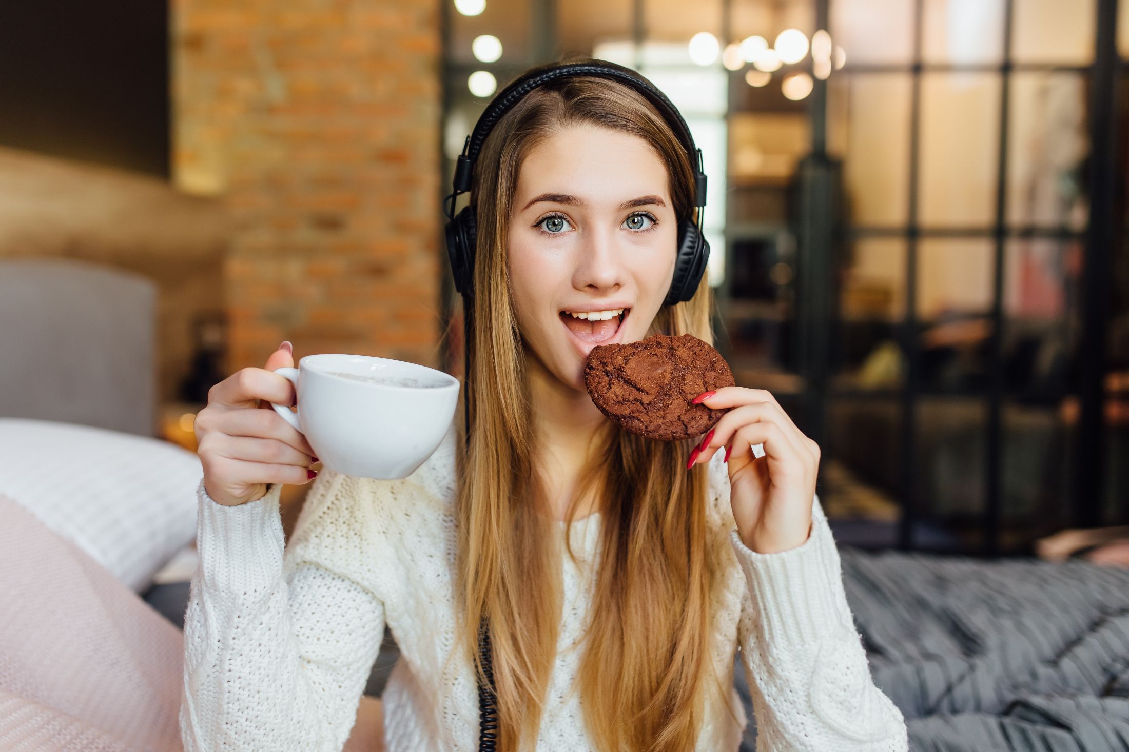 woman-smiles-while-eating-cake-drinking-coffee-and-wearing-headphone-that-connect-to-tablet-gadget.jpg
