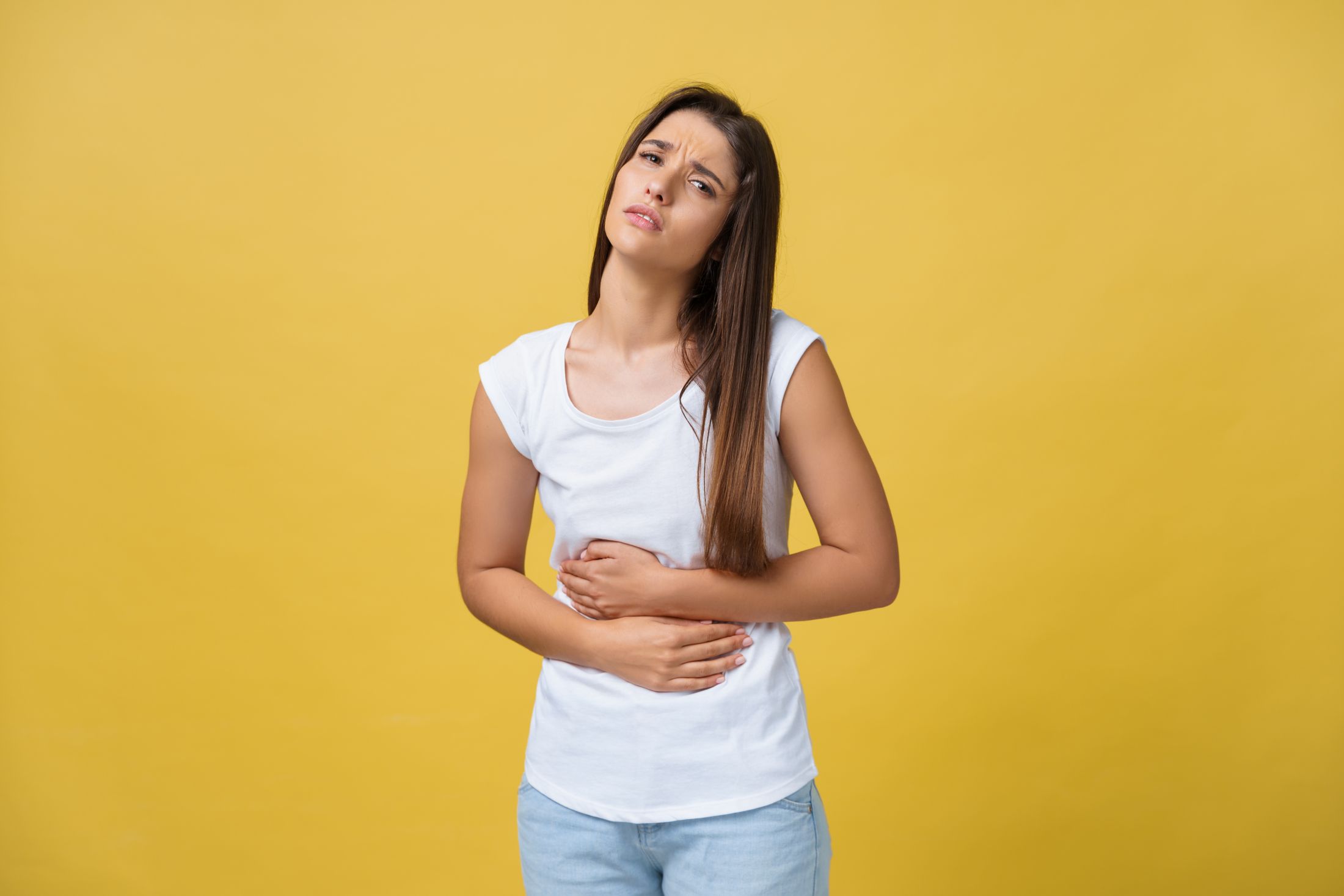 indoor-portrait-of-cute-girl-standing-with-crossed-hands-on-belly-feeling-awkward-or-suffering-from-pain-while-looking-aside-standing-against-yellow-background-woman-has-stomachache.jpg