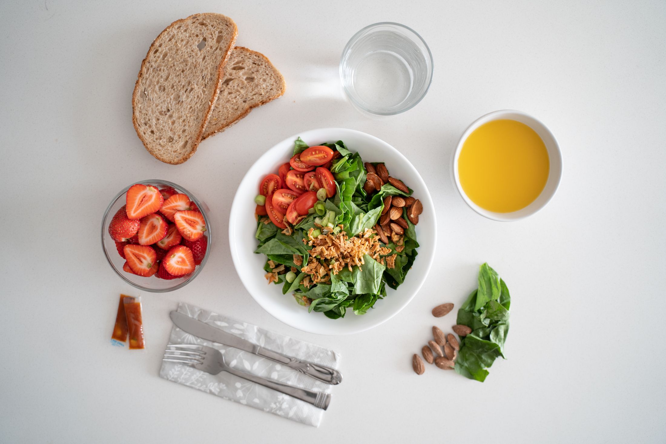 bowl-of-salad-with-herbs-tomatoes-and-almonds-on-the-table-with-strawberries-and-bread-slices.jpg