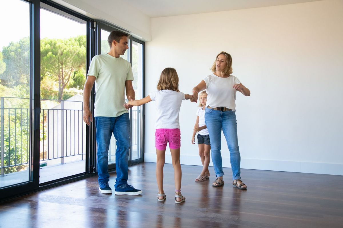 couple-of-parents-and-two-kids-enjoying-their-new-home-standing-in-empty-room-and-holding-hands-dancing.jpg