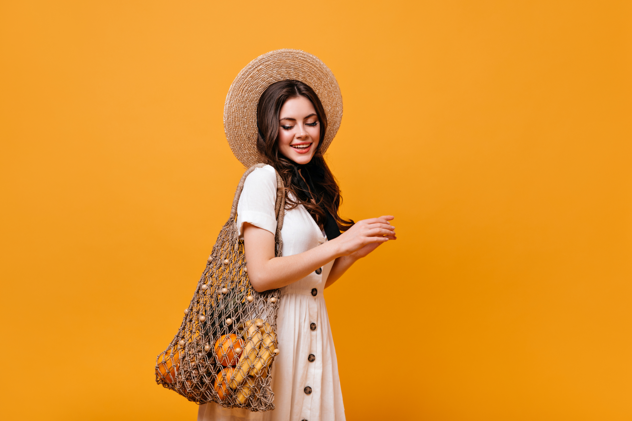 young-brunette-girl-carries-shopping-bag-with-fruit-lady-in-hat-and-white-dress-looks-down-on-orange-background.jpg