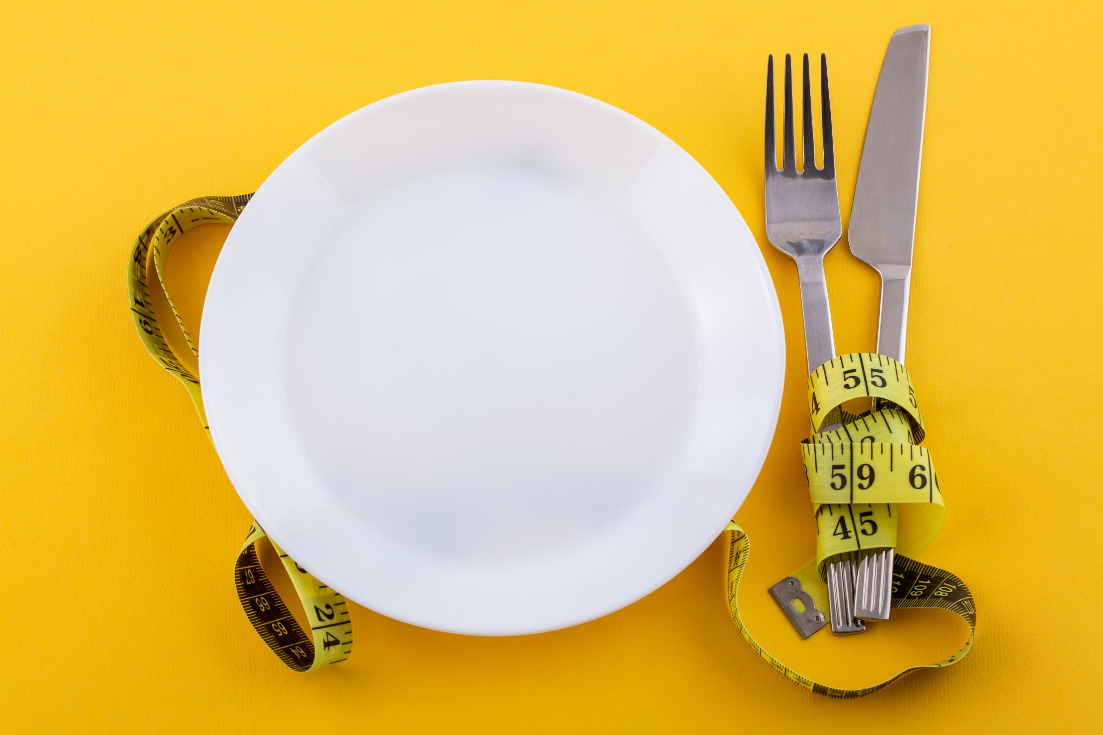 cutlery-and-a-white-plate-with-measuring-tape-on-a-yellow-the-concept-of-weight-loss-and-diet.jpg