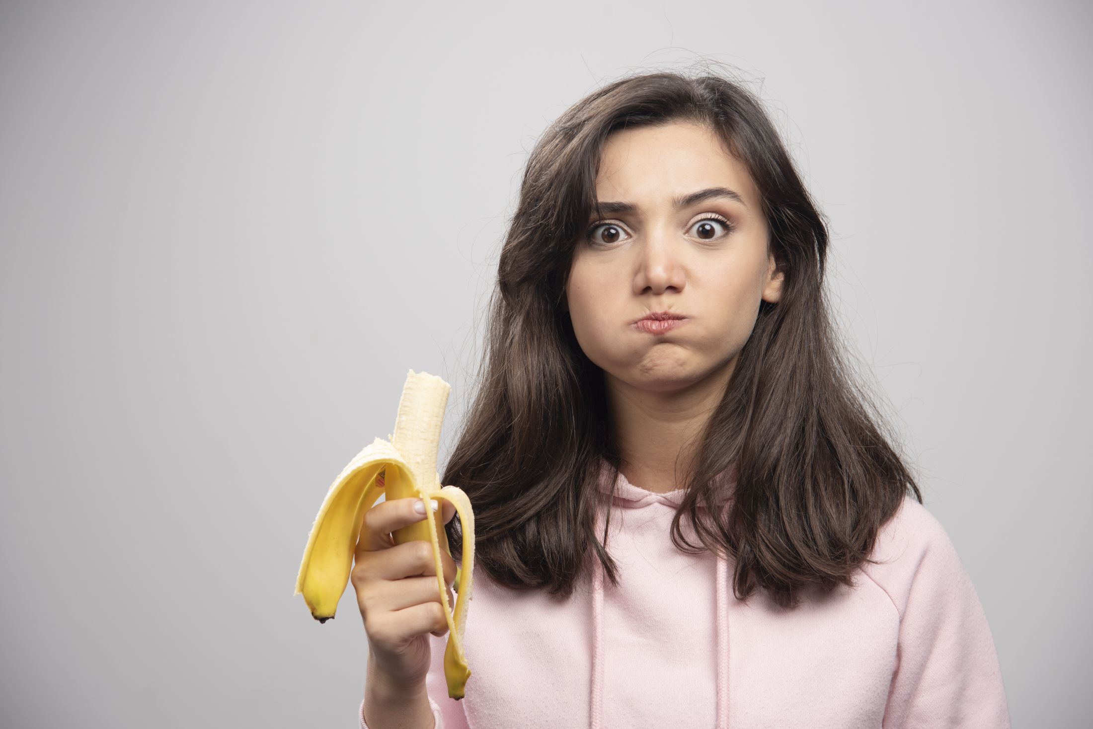young-woman-eating-banana-over-gray-wall.jpg