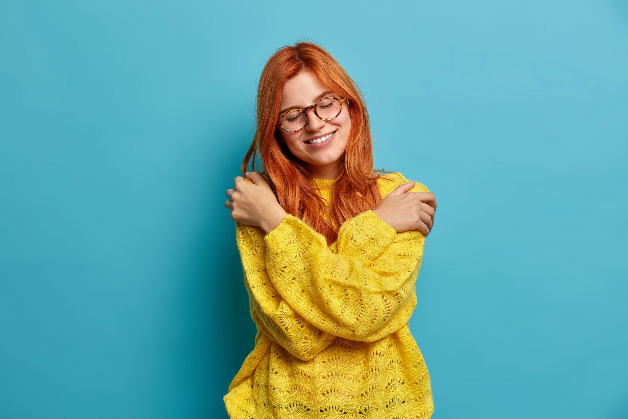 romantic-beautiful-redhead-woman-embraces-herself-expresses-self-love-and-care-tilts-head-smiles-gently-closes-eyes-hugs-own-body-wears-warm-yellow-sweater-expresses-calmness.jpg