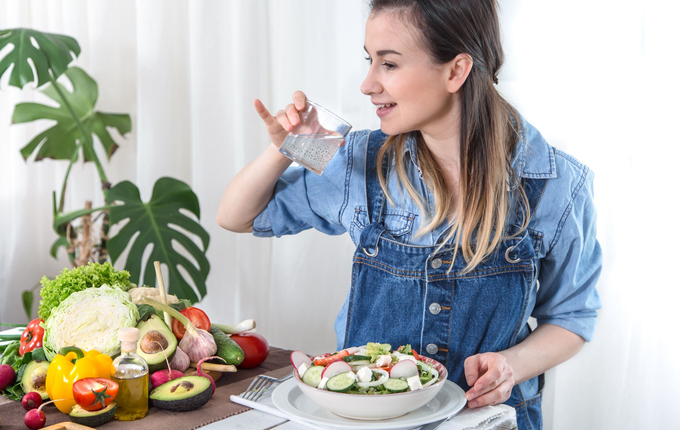 a-young-woman-drinks-water-at-a-table-with-vegetables-on-a-light-background-dressed-in-denim-clothes-healthy-food-and-drink-concept.jpg